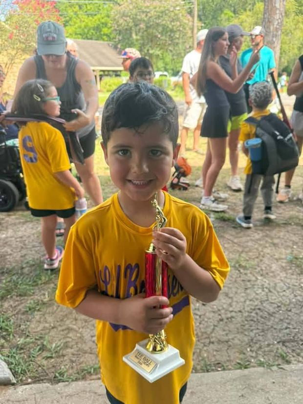 A young boy in a gold team shirt holding a trophy with a crowd behind him