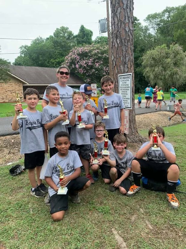 Young children in grey team shirts holding trophies under the trees