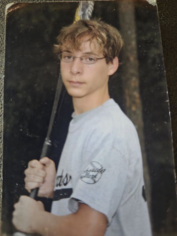 A photographed print of a teenager in a grey team shirt holding a bat in a batting pose