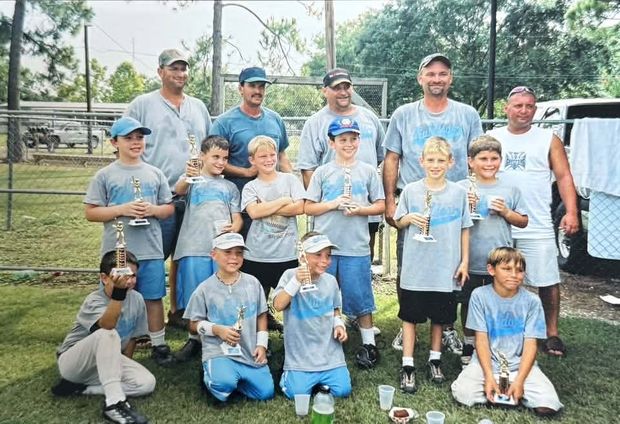 Small children in grey shirts holding trophies with adult coaches behind them