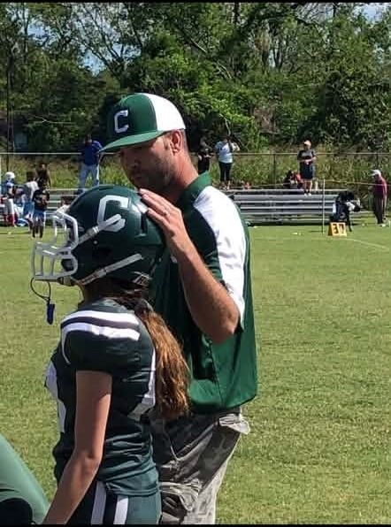 A young football player in a helmet listening to a coach at the field