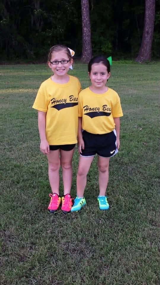Two young girls in yellow Honey Bees shirts standing together on the grass