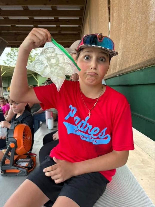 A boy in a red Padres shirt holding up a bag of ice in the dugout