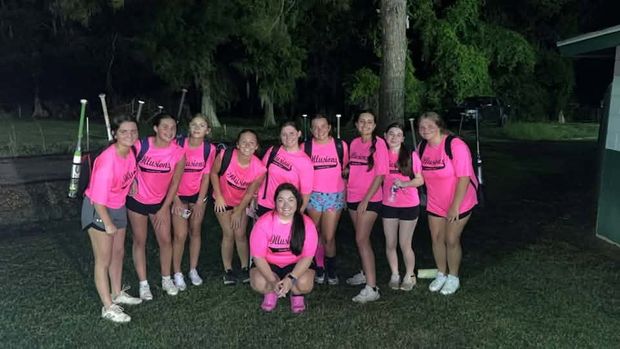 A team in pink Illusions shirts posed with bats at night