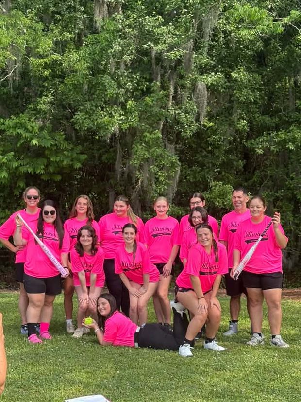 A girls team in pink Illusions shirts posed under trees hung with Spanish moss