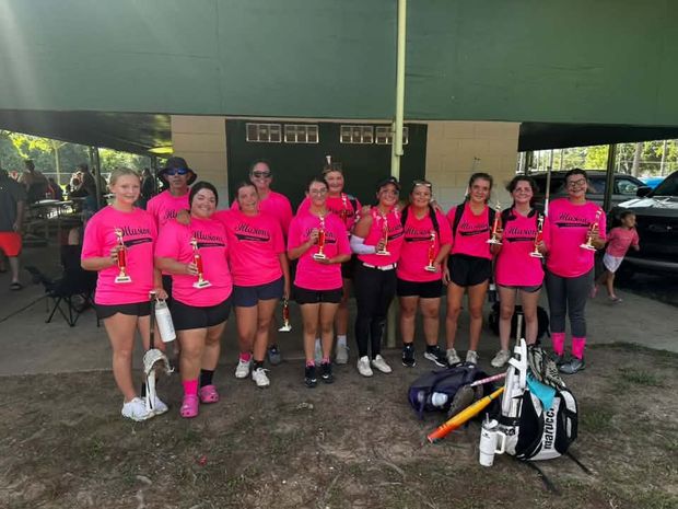 A team in pink Illusions shirts holding gold trophies under the pavilion