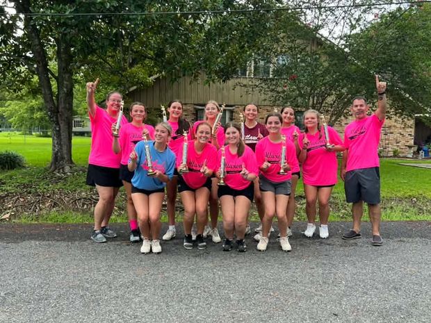 A team in pink Illusions shirts with their coaches, lined up on the road holding trophies