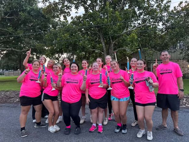 A team in pink Illusions shirts holding tall trophies