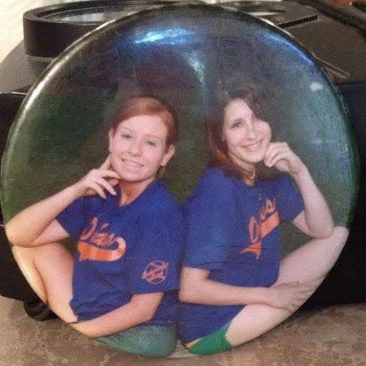A round team button showing two girls in blue Orioles jerseys sitting side by side