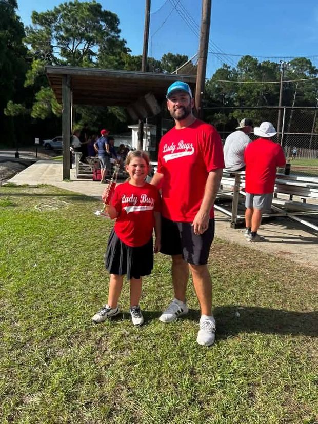 A man and a girl in matching red Lady Bugs shirts standing together on the grass