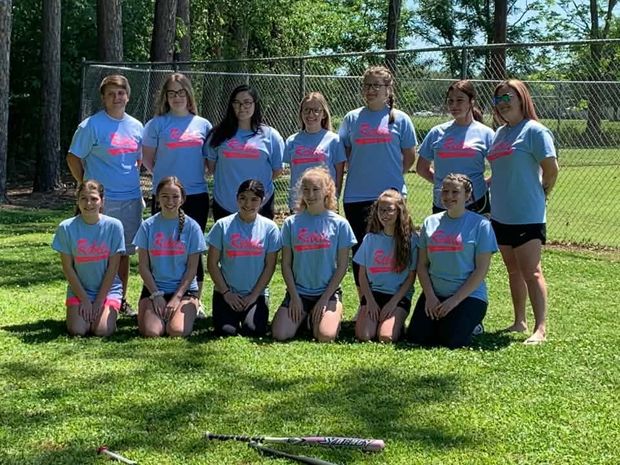A girls team in light blue shirts posed in two rows near the fence