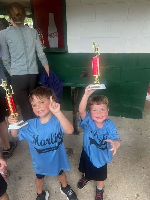 Two young boys in blue Marlins shirts raising trophies