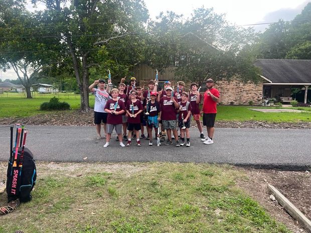 A team in maroon shirts on the drive with their arms raised, equipment bags in the foreground