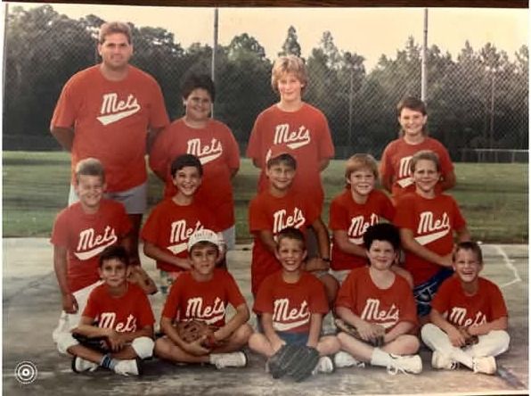 A printed team photograph of players in red Mets shirts posed in rows