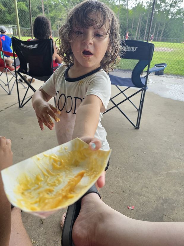 A toddler handing over an empty nacho tray under the pavilion