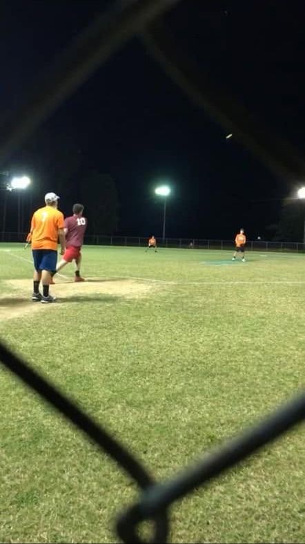 A game under the field lights at night seen through the chain link fence