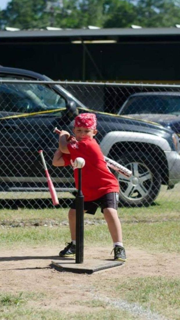 A small child in red hitting a ball off a batting tee