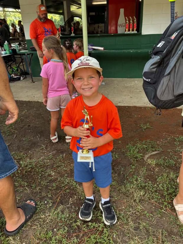 A small boy in an orange shirt holding a trophy at the concession stand