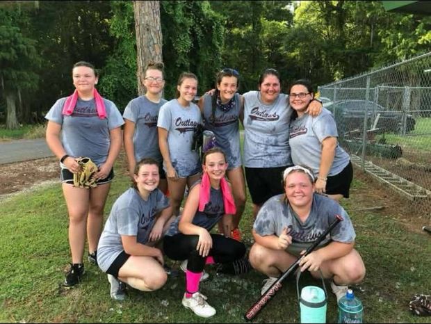 A girls team in grey Outlaws shirts posed by the fence