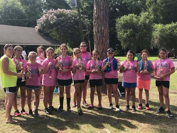 A girls team in pink shirts wearing medals and holding trophies