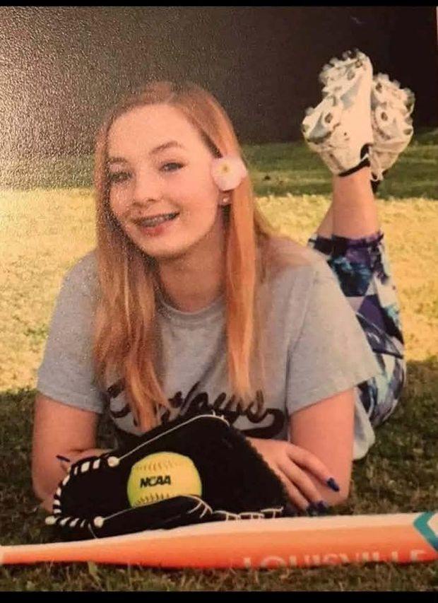 A printed portrait of a girl posed lying on the grass with a glove and softball