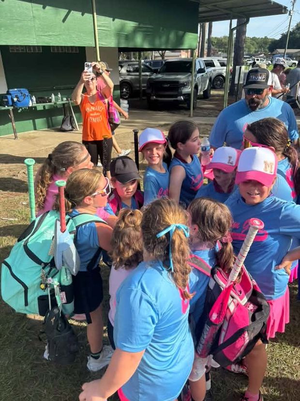 Girls in blue and pink gathered in a huddle with their backpacks and bats