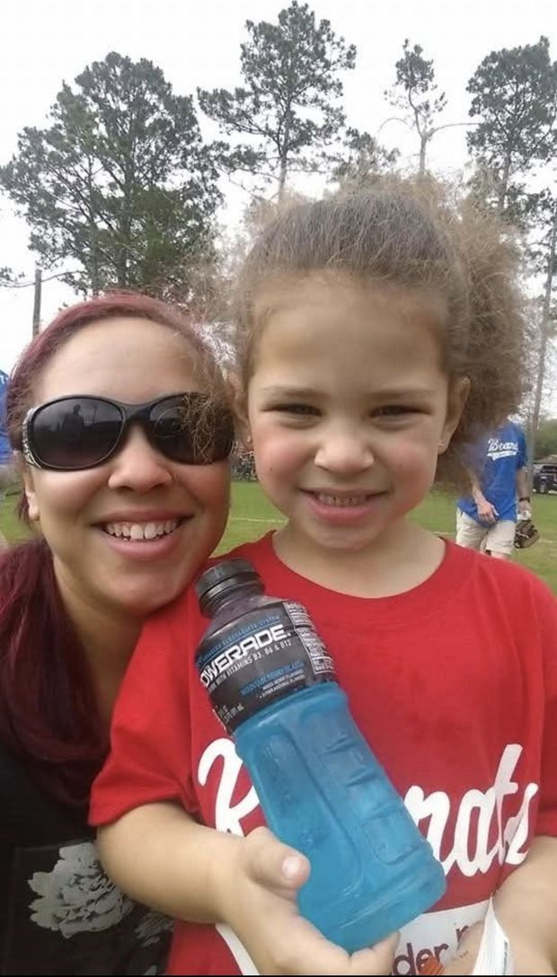 A woman in sunglasses beside a young child in a red Rebels shirt holding a blue sports drink