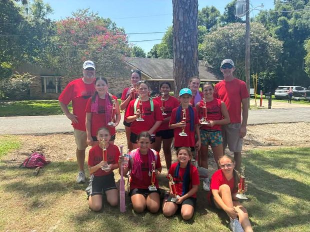 Girls in red team shirts holding trophies under a tree