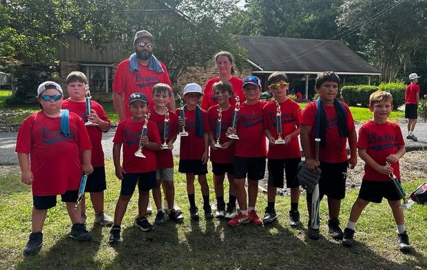 A line of children in red shirts holding trophies on the grass, with two coaches behind
