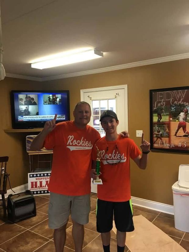 A man and a teenager in orange Rockies shirts standing together indoors with a trophy