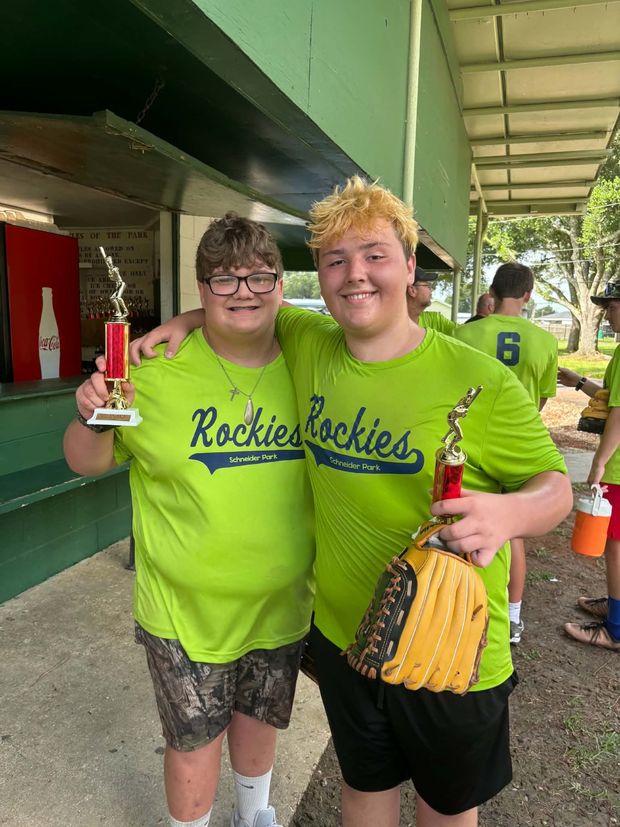 Two teenage players in neon green Rockies shirts, one holding a trophy and one a glove