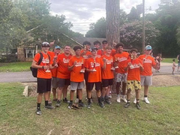 Teenage players in orange Rockies shirts holding small trophies outdoors