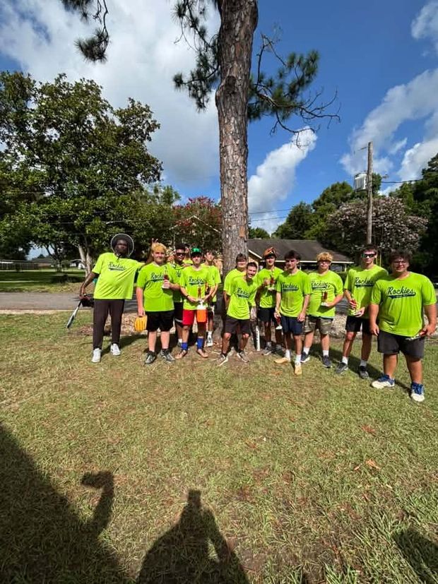 A team in neon green Rockies shirts gathered casually under a tree