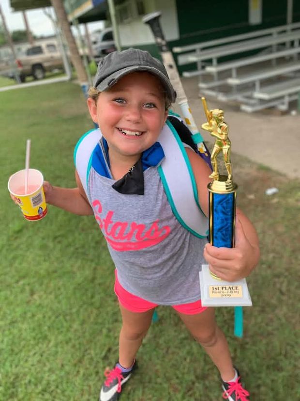 A girl in a grey Stars shirt holding a first place trophy in one hand and a drink in the other