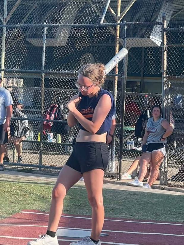A girl swinging a bat beside the fence with another player watching