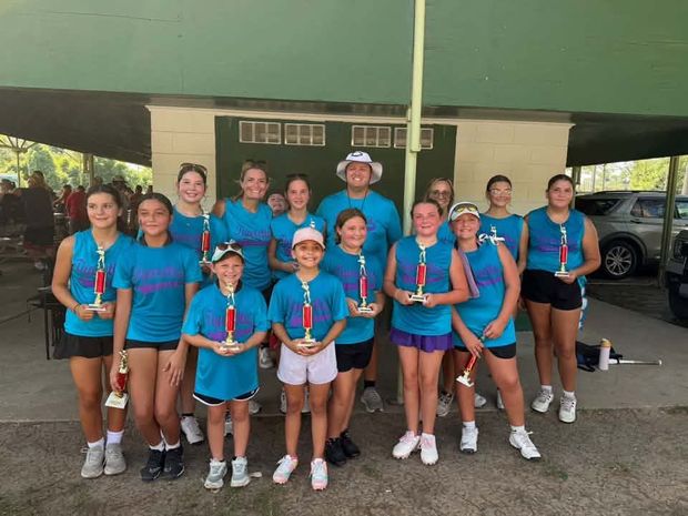 A team in teal shirts holding trophies under the covered pavilion