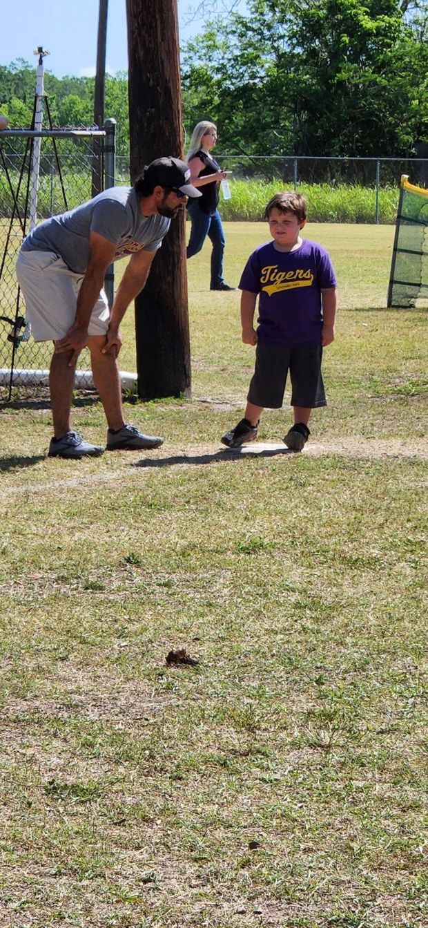 A man leaning down to coach a small child in a purple Tigers shirt near the tee