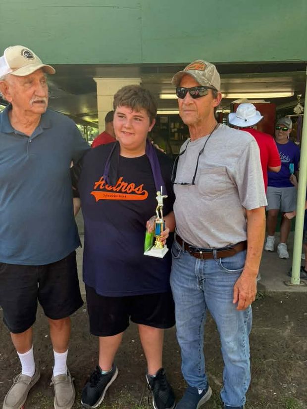 A young player holding a trophy standing between two older men under the pavilion