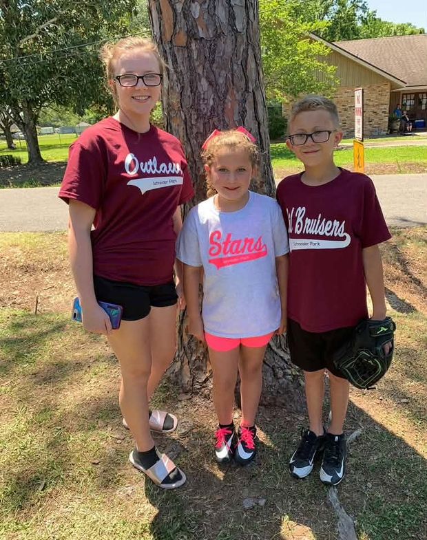 Three children in different team shirts standing together by a tree