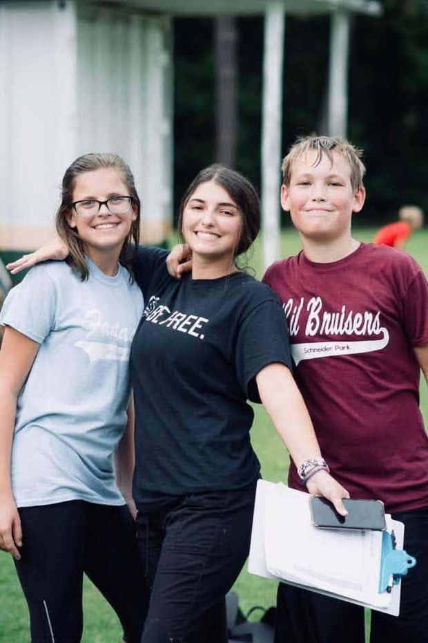 Three young people in different team shirts standing together, one holding a clipboard