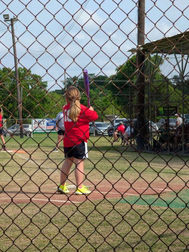 A young batter in red at the plate seen through the backstop fence