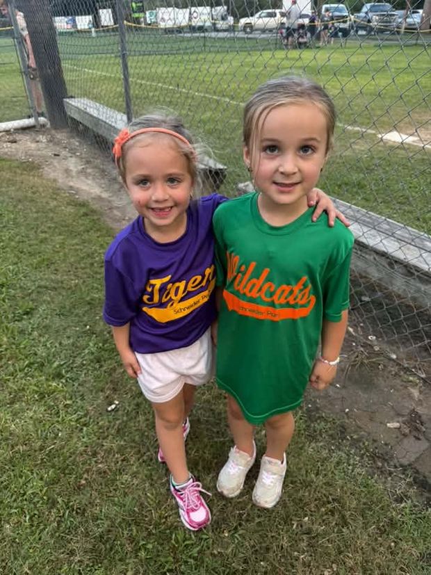 Two small girls in Tigers and Wildcats shirts standing with their arms around each other by the fence