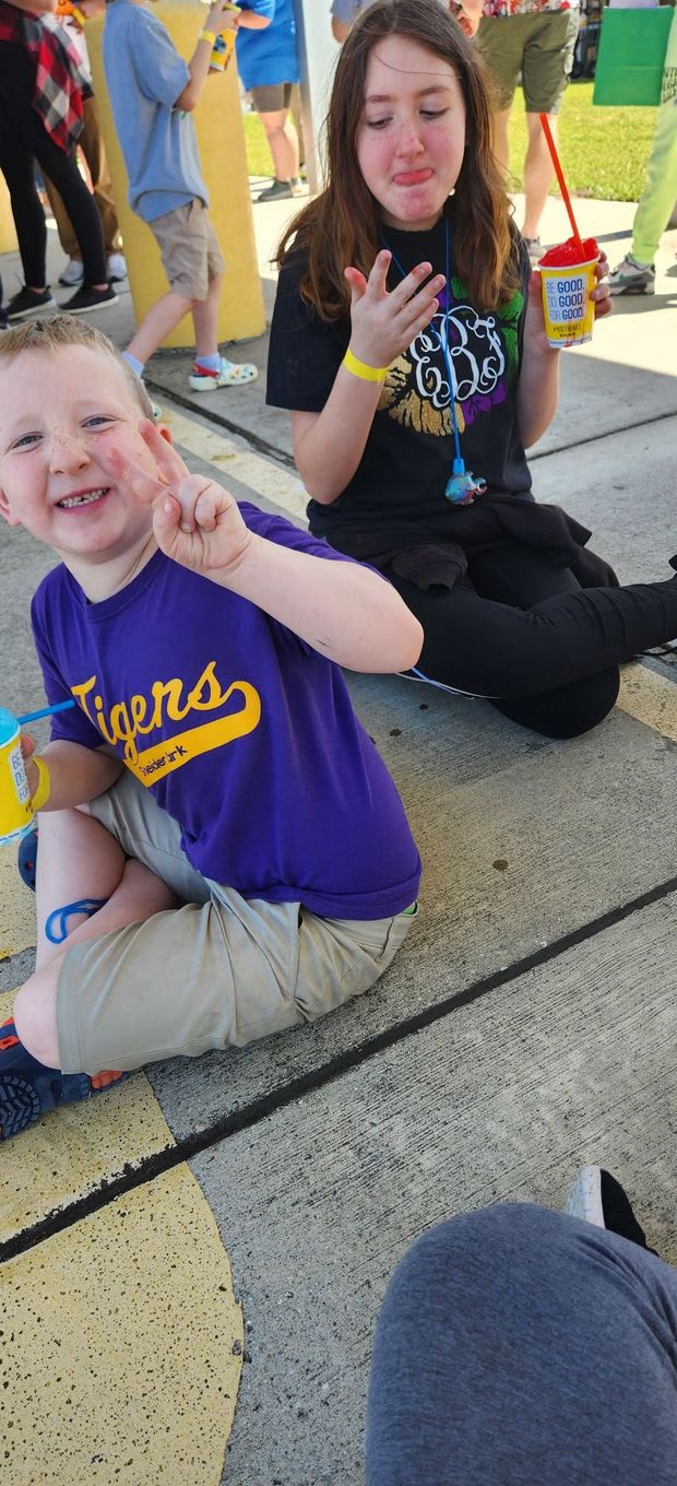 A small boy in a purple Tigers shirt sitting on the bleachers beside a teenager