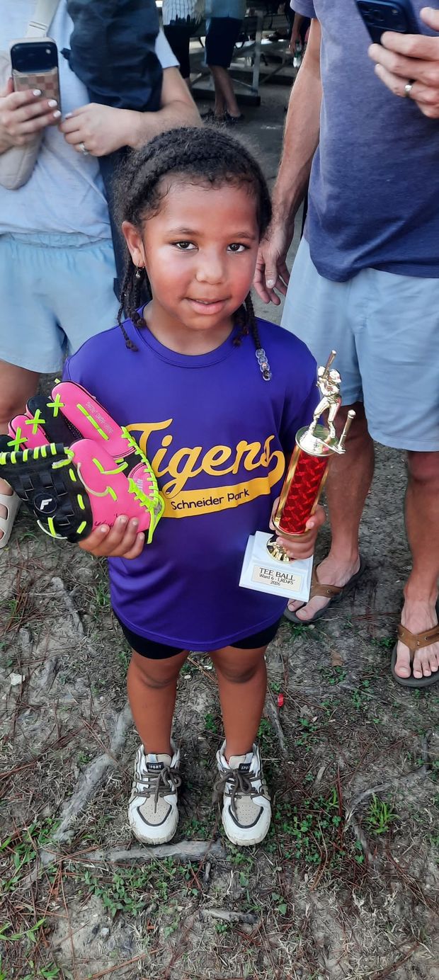 A young girl in a purple Tigers shirt holding a trophy and a pink glove