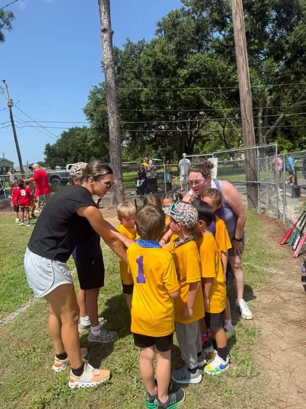A coach leaning over small children in gold shirts with their hands stacked together
