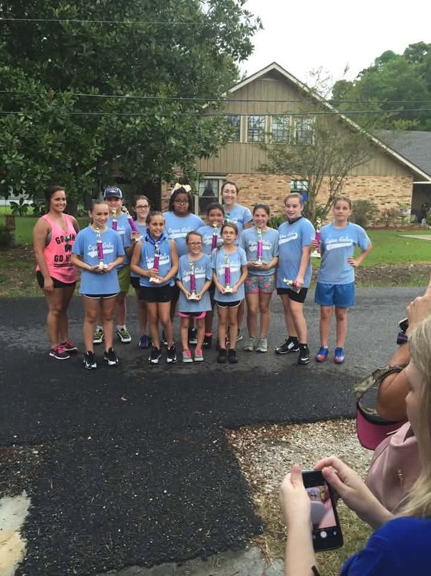A team in light blue shirts holding trophies while a parent in front photographs them with a phone
