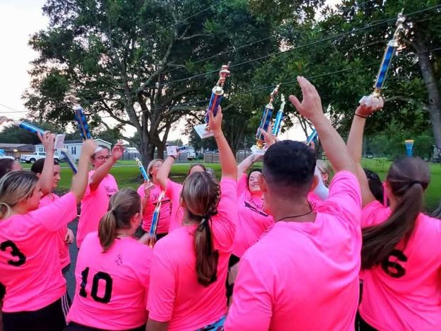 Players in pink shirts seen from behind raising their trophies overhead