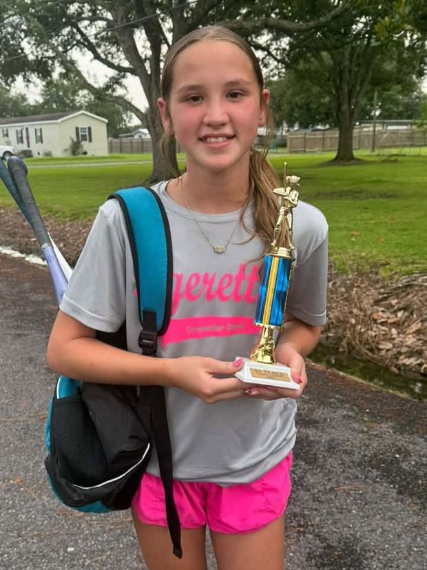 A girl in a grey team shirt holding a trophy with a bat over her shoulder