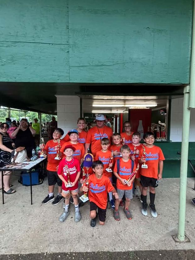 Children in orange shirts gathered at the trophy table under the pavilion