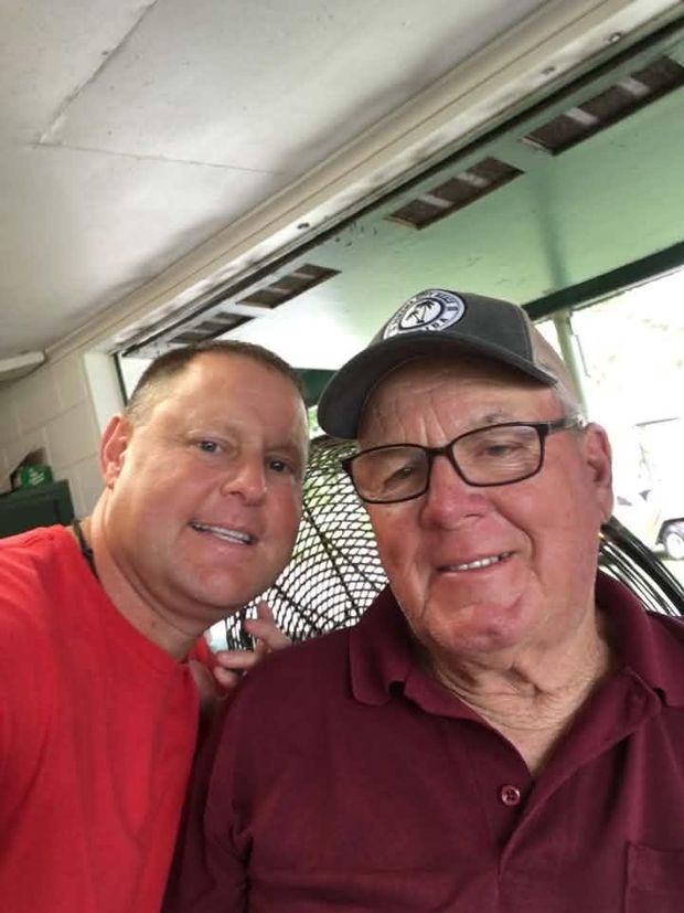 A man taking a close selfie with an older man in a maroon shirt under the pavilion